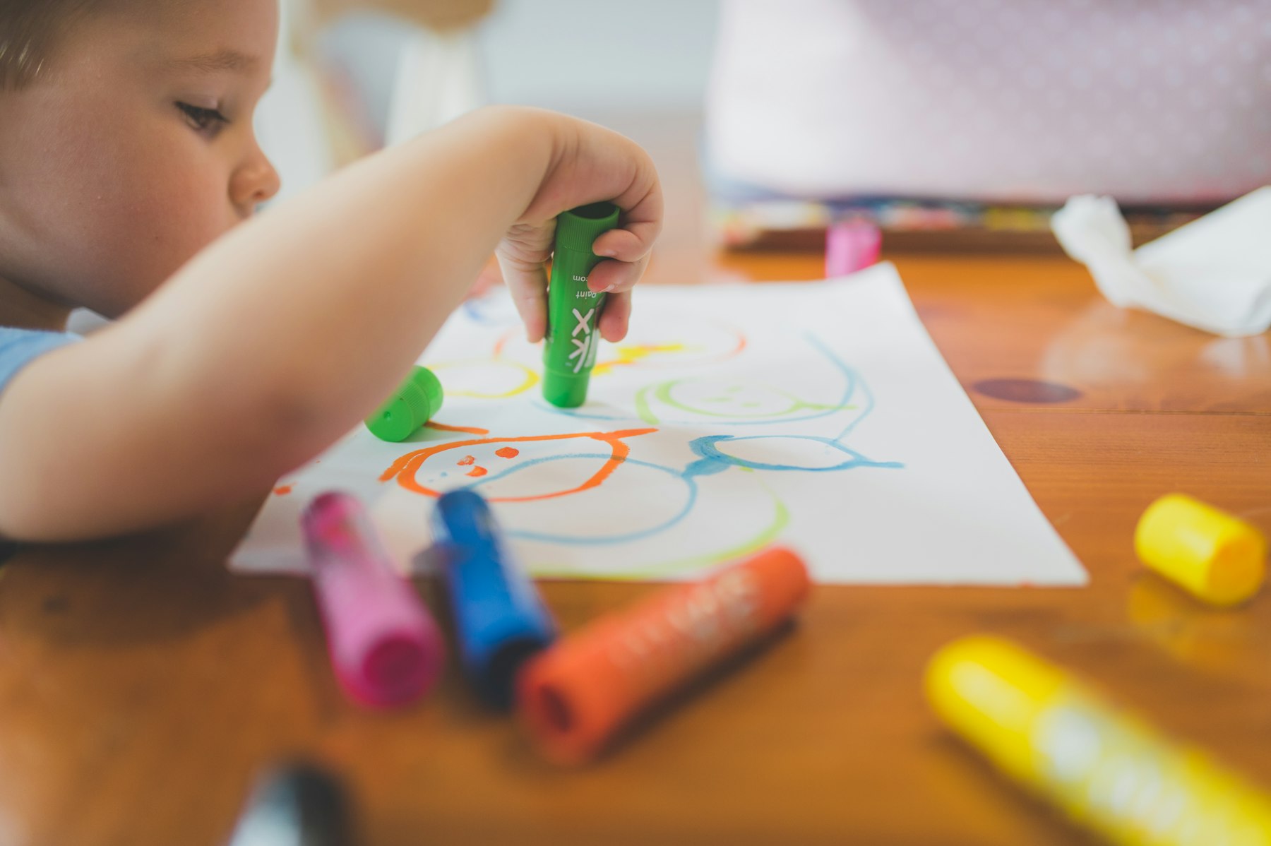 A child's hand colouring on paper with crayons at a wooden table