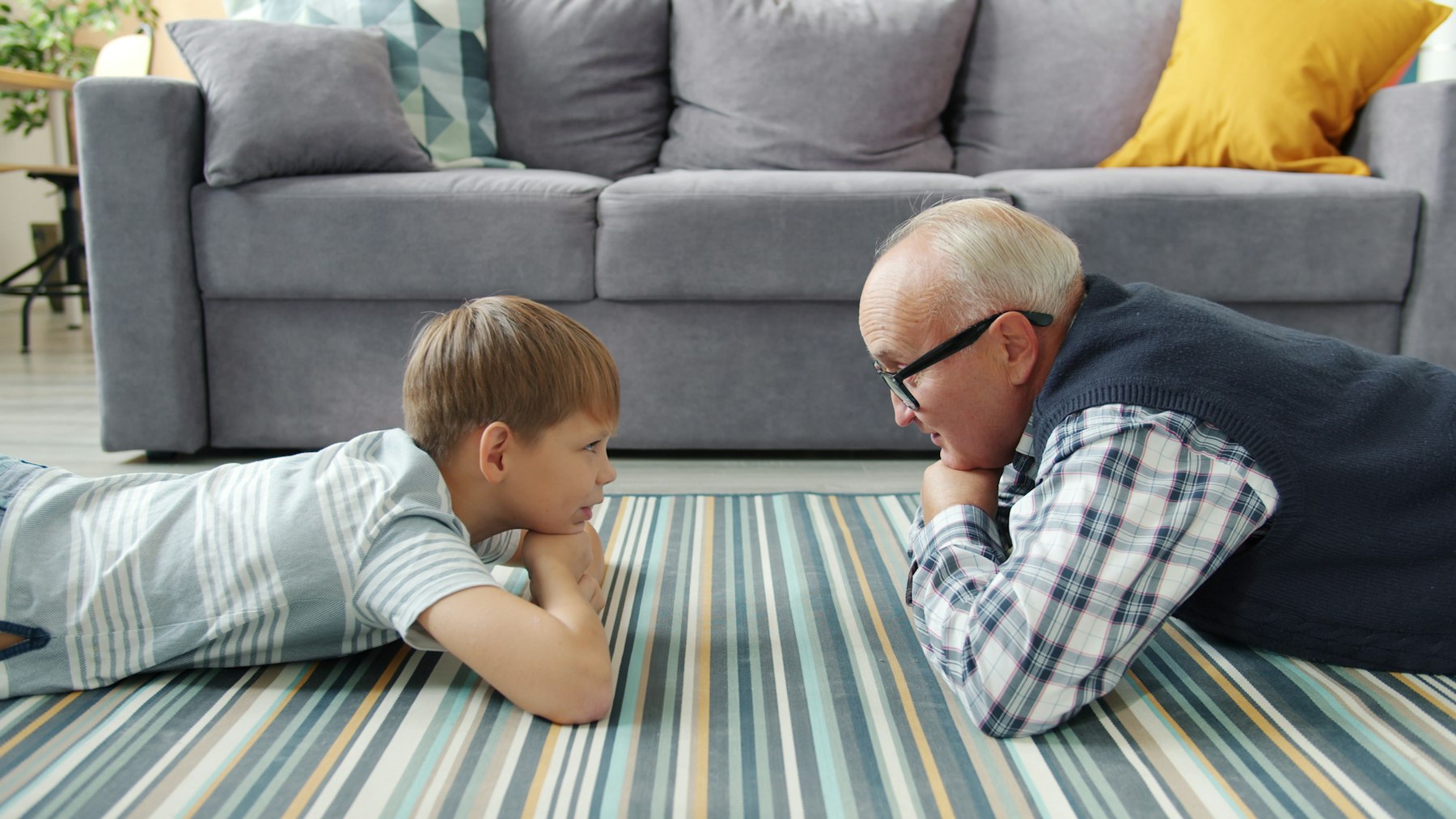 An adult and a child lie on the living room floor at eye level, talking to each other