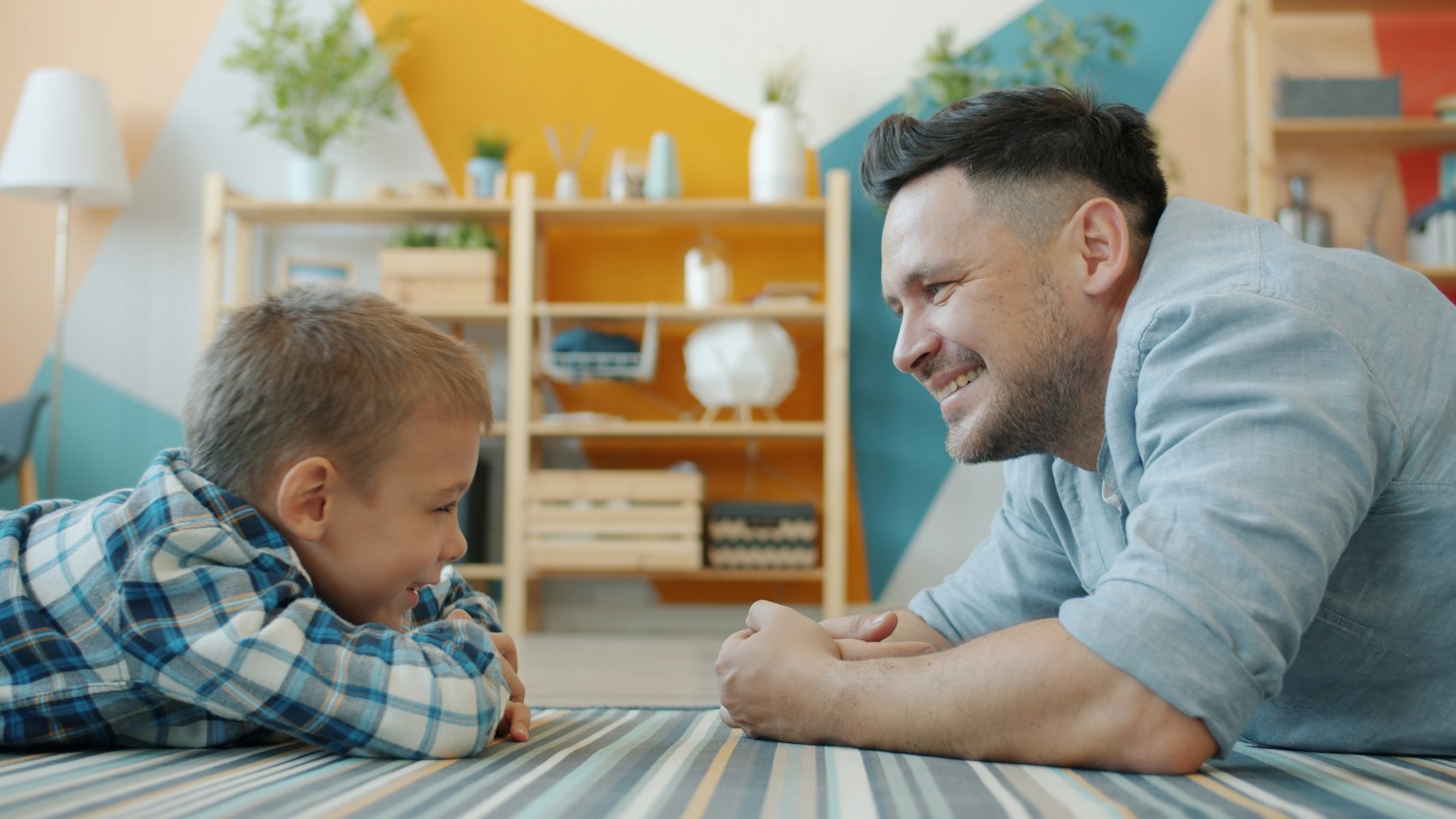 An adult lying on the floor face to face with a child, both smiling
